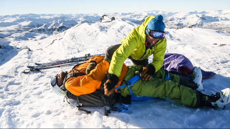 HOLD VARMEN: Det viktigste redskapet du har med i fjellet er hodet, mener Per Ola Seim i Hemsedal Skipatrulje. Programleder Jørgen Aamot demonstrerer hvordan en skadet person kan støttes opp og løftes opp fra bakken for å holde på kroppvarmen så godt som mulig. Stikkordet er improvisasjon. Bilde: Benjamin Hjort