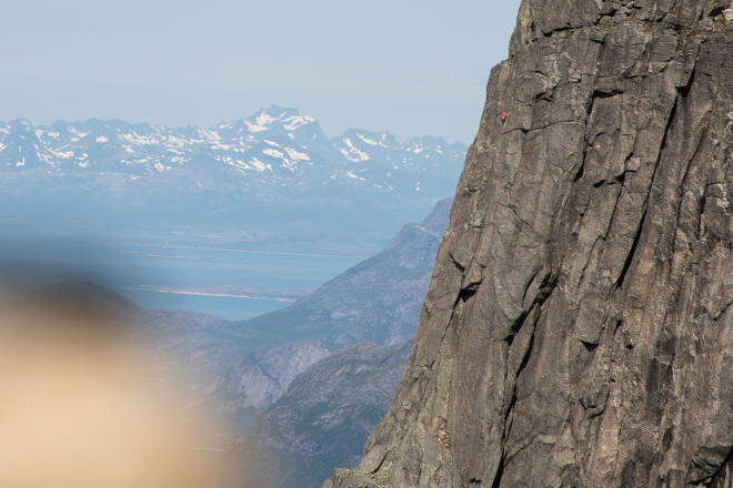 En klatrer i rød jakke på Sydpilaren med Lofotveggen i bakgrunnen og varden på Halls fortopp (1 314 moh) i forgrunnen.Foto: Tore Meirik klatring Stetind