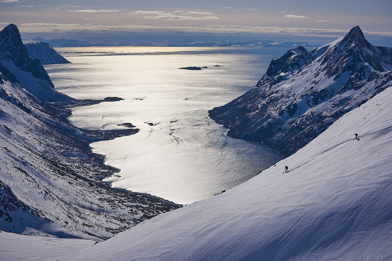BLÅFJELL OG BLÅ FJORD: Lykkelig er den som har funnet en slik flanke! Utsikten strekker seg helt ut til Andøya og fotografen nyter den og de nydelige linjene skikjørerne tegner. De to på ski har nok blikket mer fokusert i fartsretningen og sloss innbyrdes om førstespor. Foto: Svein Petter Aagard topptur på senja indre selfjord